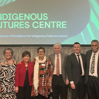 A group of men and women stand side by side on stage with a slide behind them reading Indigenous Futures Centre.